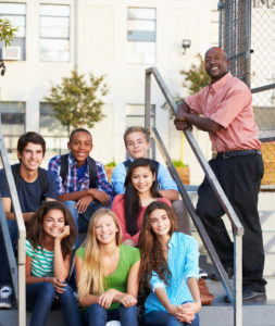 Group Of Teenage Pupils Outside Classroom With Teacher Looking At Camera Smiling